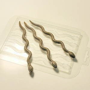 Könnte beinhalten: Eine transparente Plastikform mit vier braunen schlangenförmigen Silikonformen. Die Formen sind wellenförmig.