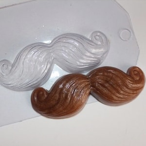May include: A clear plastic mold for making chocolate moustaches. The mold shows a brown chocolate moustache in the foreground and a white chocolate moustache in the background.