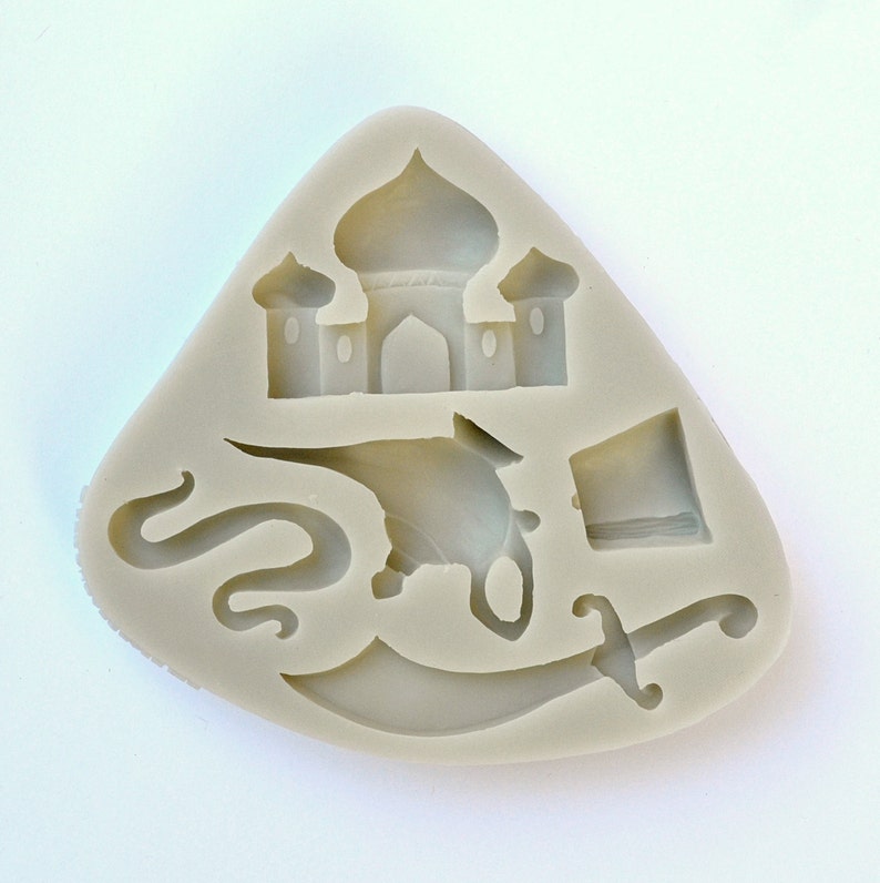 May include: A silicone mold for baking, featuring a design of a mosque, a genie, a scimitar, and a turban. The mold is light gray and has a triangular shape.