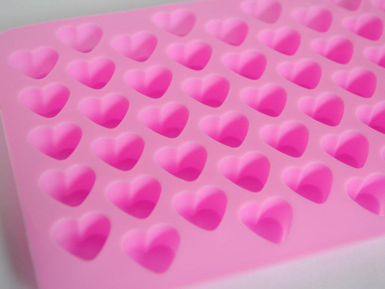 Puede incluir: Primer plano de un molde de silicona rosa con m&uacute;ltiples cavidades en forma de coraz&oacute;n. El molde es de un tono rosa vibrante, y cada coraz&oacute;n est&aacute; en relieve, creando un efecto tridimensional. Los corazones est&aacute;n espaciados uniformemente.