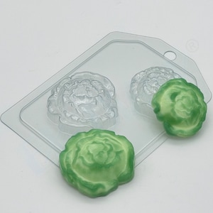Puede incluir: Un molde de plástico transparente con tres cavidades en forma de flor. Se muestran dos flores de resina verde fuera del molde.