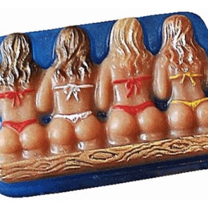 May include: Four figures in a row, each wearing a bikini, sitting on a wooden platform. The figures are made of a light brown material and have long blonde hair. The bikinis are in different colors: red, white, yellow, and red.