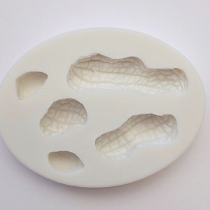 May include: White silicone mold with four peanut shapes. The mold is designed to create peanut-shaped candies or decorations.