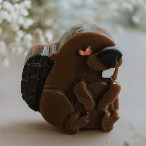 Puede incluir: Una figurita de castor marrón y negro con una sonrisa de dientes. El castor está sentado con las patas delante.