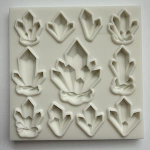 Peut inclure: Un moule en silicone blanc présentant neuf motifs de cristaux. Les cristaux varient en taille et en forme, avec des facettes géométriques et pointues. Le moule est carré et a une surface lisse, idéal pour le bricolage ou la pâtisserie.