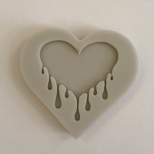 May include: A gray silicone mold shaped like a heart with a dripping heart design inside.
