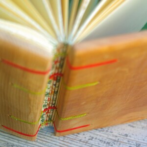 May include: A wooden journal with a natural wood cover and colorful string accents. The journal is open to reveal the pages inside.