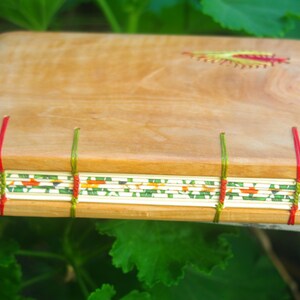 May include: A wooden journal with a natural wood cover and a decorative stitched design. The journal has a green, red, and white patterned paper spine.
