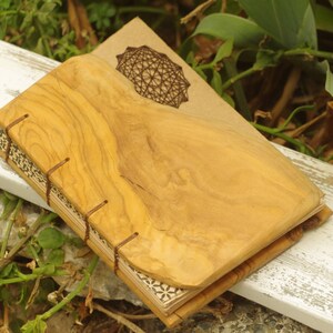 May include: A handmade journal with a wooden cover and a geometric design on the front. The cover is made of natural wood and has a rustic look. The journal is perfect for writing, journaling, or sketching.