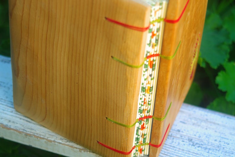 May include: A wooden book with a decorative spine featuring a colorful pattern of red, green, and white. The book is bound with red and green thread.