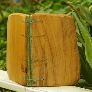 May include: A wooden journal with a natural wood cover and a spine bound with blue and green thread. The journal is sitting on a white surface.