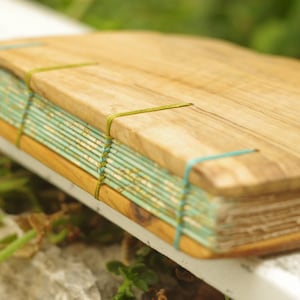 May include: A wooden-cover journal with a turquoise and white patterned paper spine. The journal is bound with green string.