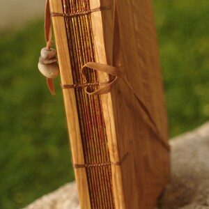 May include: A wooden journal with a leather strap and a decorative stone charm. The journal has a red and gold patterned cover.