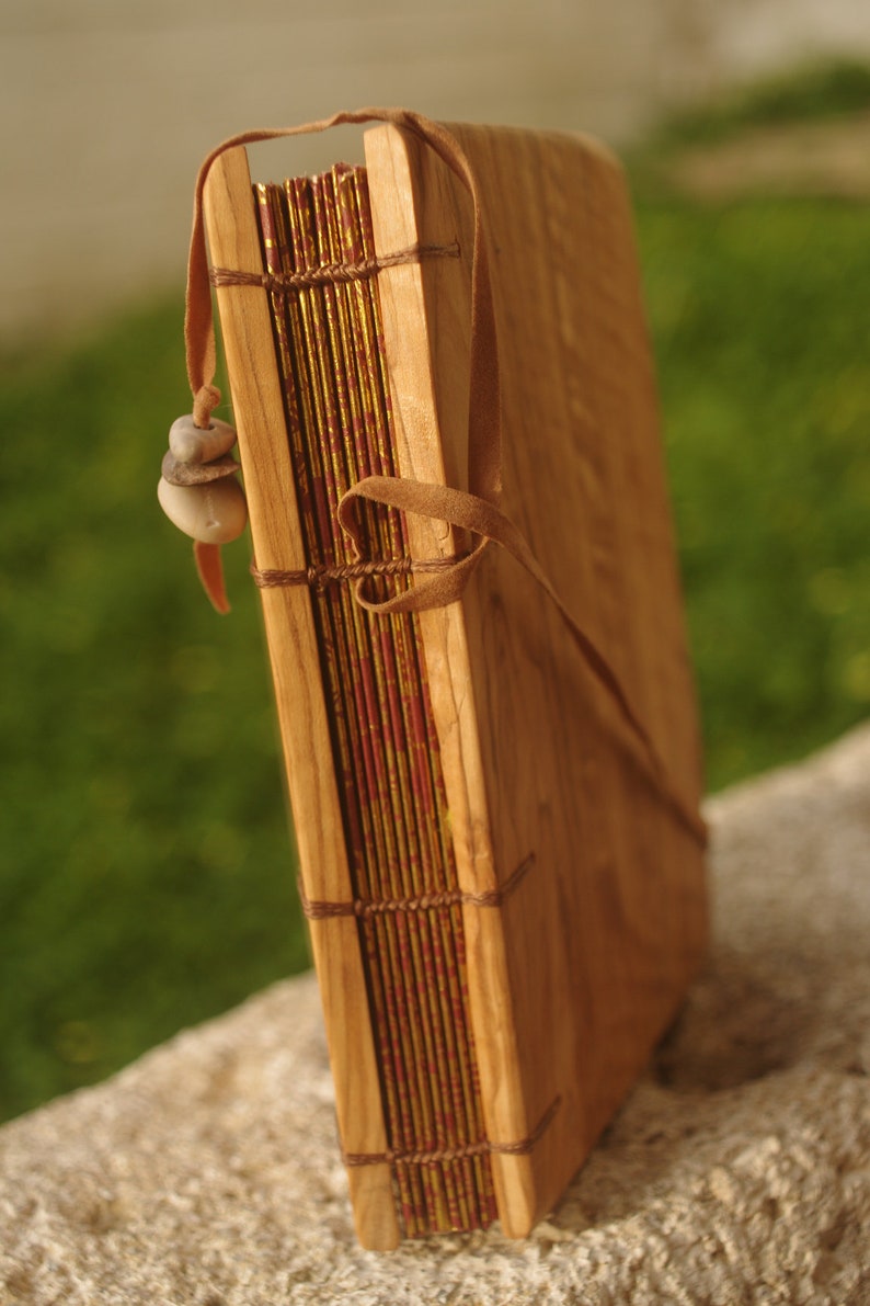 May include: A wooden journal with a leather strap and a decorative stone charm. The journal has a red and gold patterned cover.
