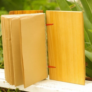 May include: A wooden journal with a brown paper cover and red string closure. The journal is open to reveal blank pages.