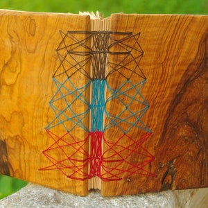 May include: A wooden journal with a geometric design stitched into the cover using red, blue, and black thread.