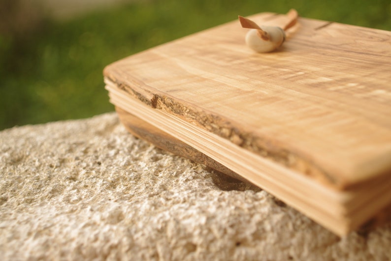 May include: A wooden cutting board with a natural edge and a light brown color. The board is made of multiple layers of wood and has a rustic look.