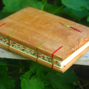 May include: A handmade journal with a wooden cover and red and green stitching. The cover has a natural wood grain pattern.