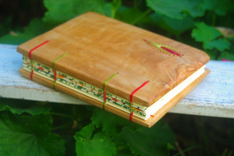 May include: A handmade journal with a wooden cover and red and green stitching. The cover has a natural wood grain pattern.