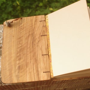 May include: A wooden journal with a natural wood cover and a decorative gold and red spine. The journal is open to a blank page.