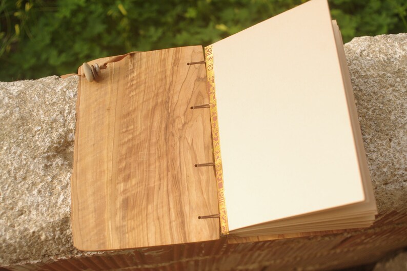 May include: A wooden journal with a natural wood cover and a decorative gold and red spine. The journal is open to a blank page.