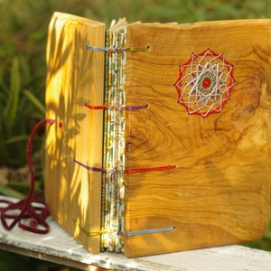 Könnte beinhalten: Ein Holzjournal mit einem bunten Schnurschluss und einem roten, weißen und grünen String-Art-Design auf dem vorderen Umschlag.