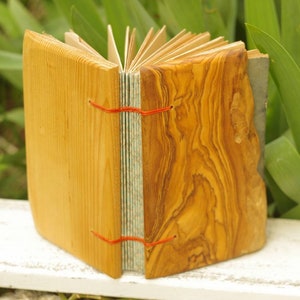May include: A handmade journal with a wooden cover. The cover is made of two different types of wood, one light and one dark. The journal is closed and tied with red string.