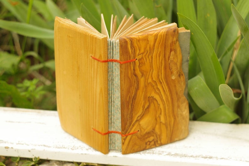 May include: A handmade journal with a wooden cover. The cover is made of two different types of wood, one light and one dark. The journal is closed and tied with red string.