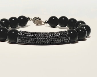 Puede incluir: Un brazalete de cuentas negras con una barra de metal negro incrustada con pequeñas piedras negras.