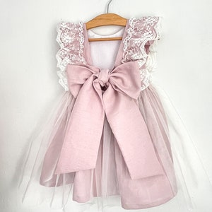 May include: A pink tulle dress with a large pink satin bow on the back. The dress has white lace trim on the shoulders.