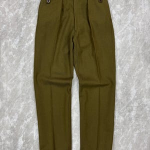 May include: Olive green trousers featuring a high-waisted design with double pleats at the front. The waistband includes side adjusters with dark buttons and tabs, creating a structured look with straight legs and a clean, pressed crease down each leg.