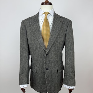 Può includere: Un blazer grigio a spina di pesce con chiusura a due bottoni. Il blazer ha una tasca sul petto e due tasche anteriori.