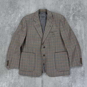 Puede incluir: Una chaqueta de traje de cuadros marrones, negros y beige con cierre de dos botones.