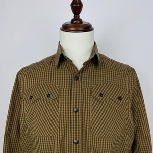 May include: A long-sleeved, button-down shirt in a brown and olive green checkered pattern. The shirt features two chest pockets with button closures and a classic collar. The shirt is displayed on a mannequin.