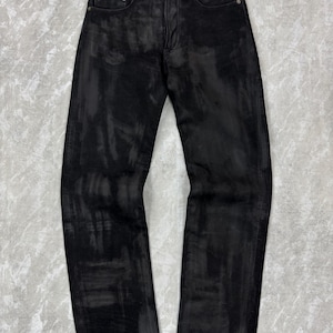 May include: Black denim jeans featuring a distressed, washed-out aesthetic with lighter grey streaks throughout the fabric. These trousers include a standard button fly closure, five pockets, and a straight-leg cut with a clean, finished hemline.