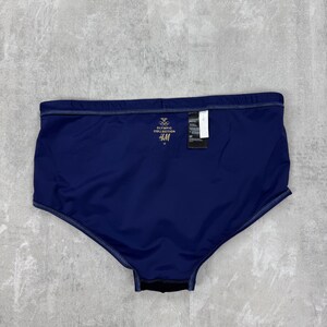 May include: Navy blue swim trunks with a tag. The trunks have a high waist and a dark blue color. The tag reads "Olympic Collection" and "H&M".