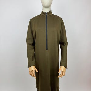 Könnte beinhalten: Ein langärmeliges, olivgrünes Kleid mit einem schwarzen Reißverschluss an der Vorderseite. Das Kleid hat einen hohen Ausschnitt und eine lockere Passform.