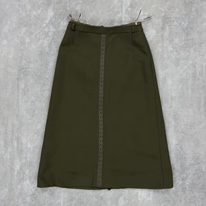 Op de afbeelding: Olijfgroene rok met een rechte snit. De rok heeft een decoratieve, verticale, lichtgekleurde bies in het midden. De tailleband heeft riemlussen en is gevoerd met een contrasterende stof. De rok hangt aan een hanger.