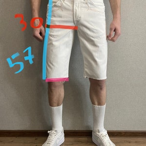 May include: White denim shorts with a frayed hem. The shorts have a 30 inch waist and a 57 inch inseam. The shorts are being worn by a person with white socks and white sneakers.