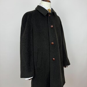 May include: A dark gray wool coat with a classic design. The coat features a collared neckline, three brown buttons, and two front pockets. The coat is displayed on a mannequin, showcasing its tailored fit and style. The coat's length extends to mid-thigh.