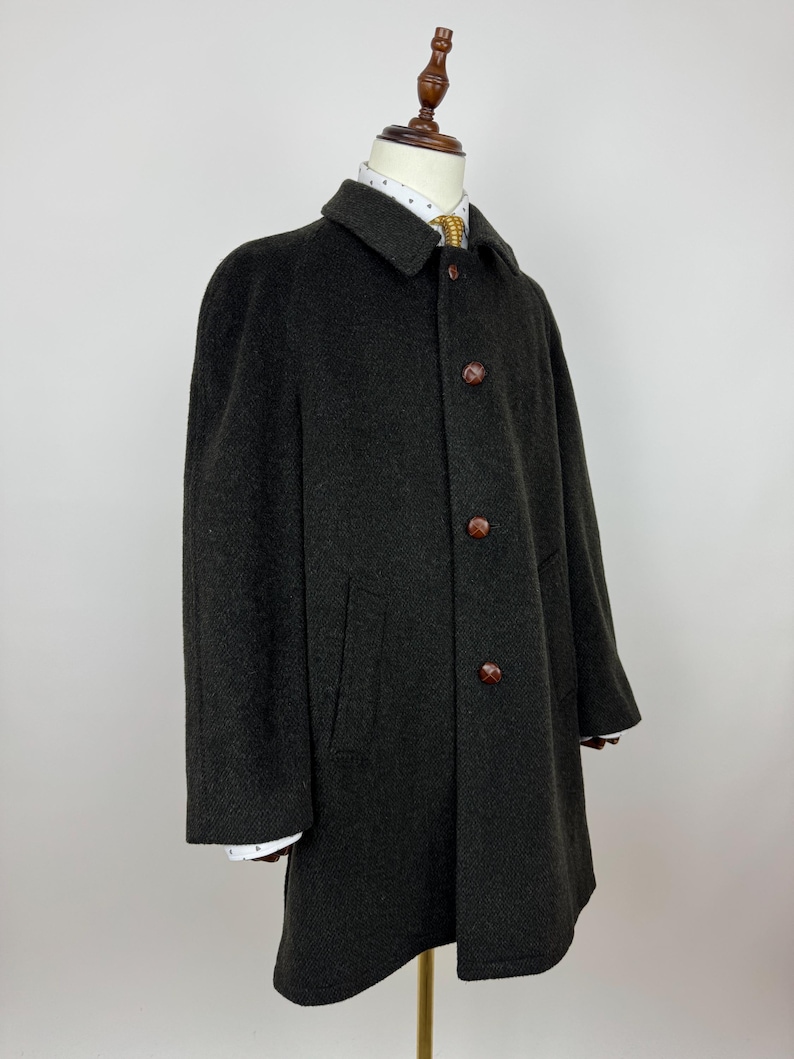 May include: A dark gray wool coat with a classic design. The coat features a collared neckline, three brown buttons, and two front pockets. The coat is displayed on a mannequin, showcasing its tailored fit and style. The coat's length extends to mid-thigh.