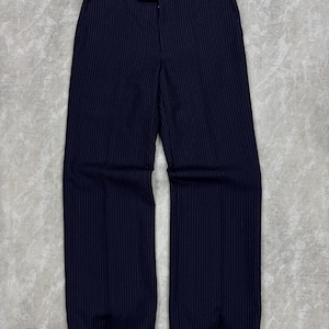 May include: Navy blue pinstripe trousers. The pants have a wide leg design and a classic tailored look. The pinstripes are vertical and thin, adding a subtle pattern to the dark blue fabric. The trousers are neatly pressed and appear to be made of a smooth material.