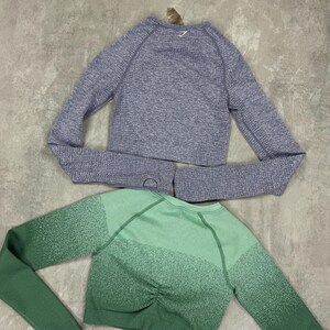 May include: Three long-sleeved crop tops in shades of gray, green, and burgundy. The gray top has a textured knit, while the green top features a gradient effect. Each top has a crew neck and thumb holes. The tops are designed for athletic wear.