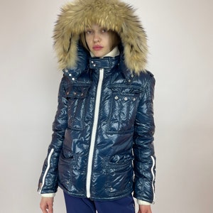 Puede incluir: Una chaqueta acolchada azul marino con una cremallera blanca y detalles blancos. La chaqueta tiene una capucha de piel sint&eacute;tica y un dise&ntilde;o acolchado.