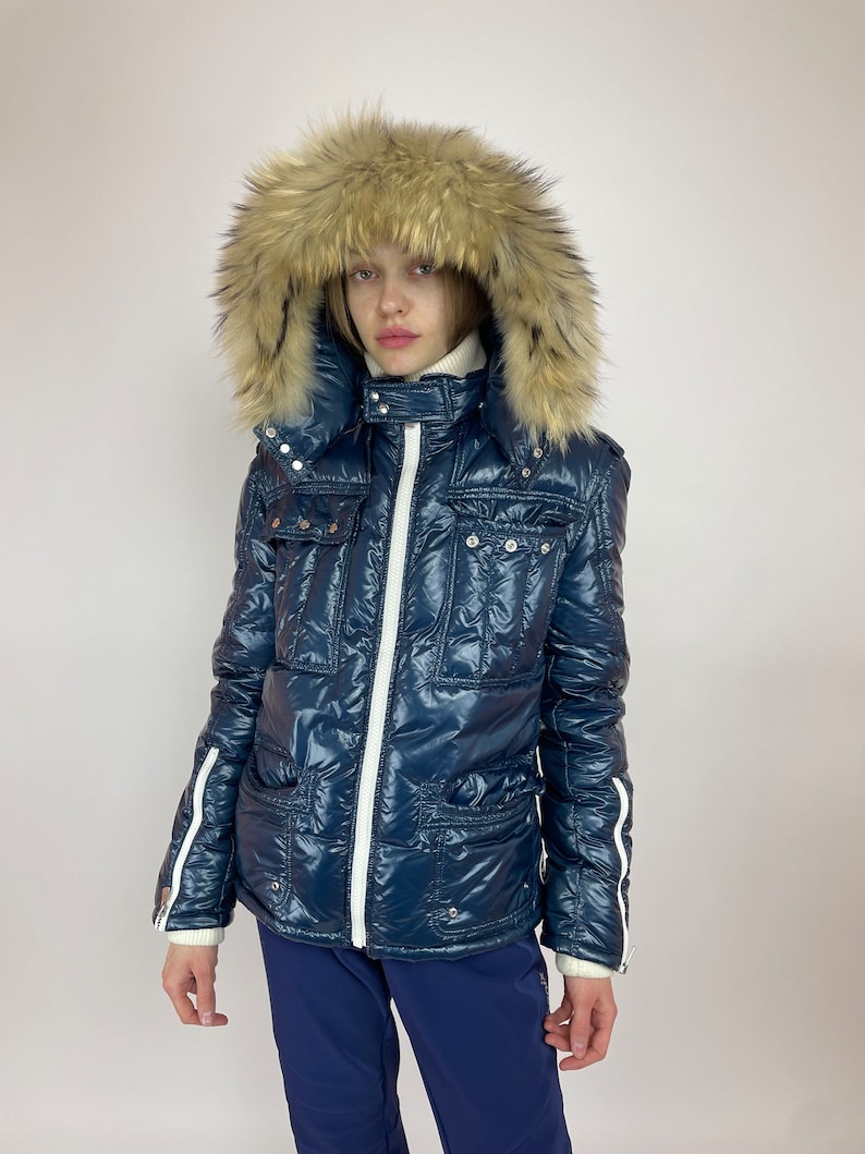 Puede incluir: Una chaqueta acolchada azul marino con una cremallera blanca y detalles blancos. La chaqueta tiene una capucha de piel sint&eacute;tica y un dise&ntilde;o acolchado.