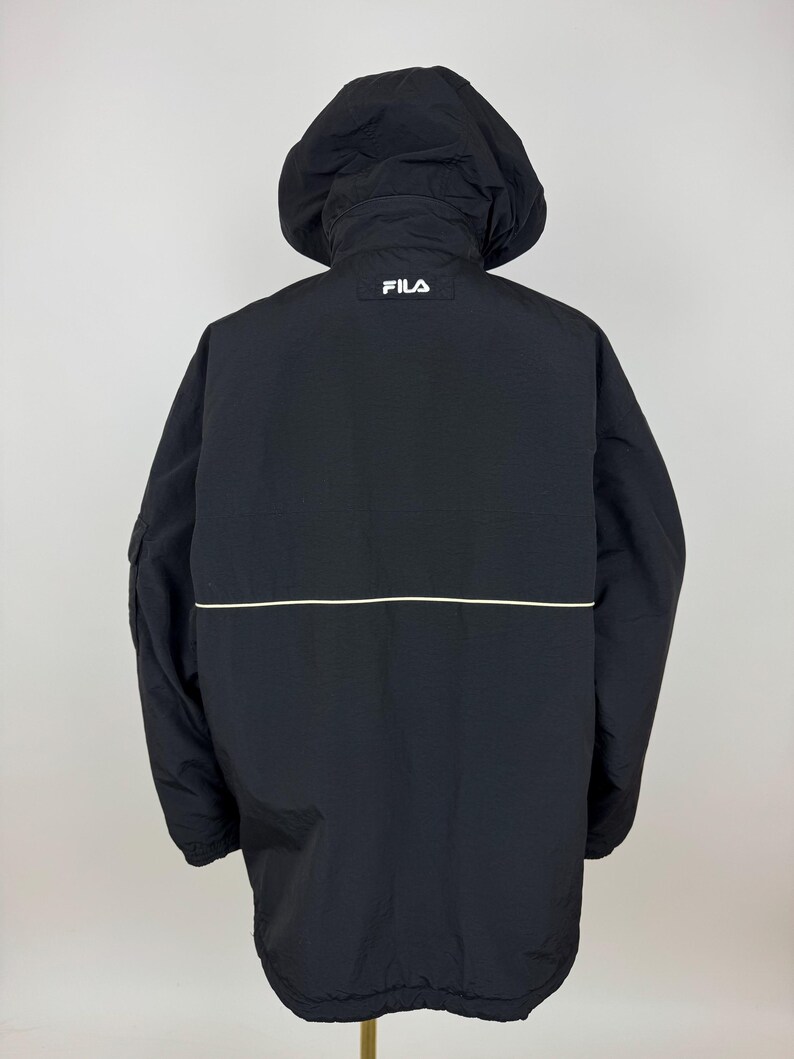 Puede incluir: Chaqueta negra con capucha y el logotipo blanco "FILA" en la parte superior de la espalda. La chaqueta tiene una raya horizontal blanca en la espalda y una capucha. La chaqueta est&aacute; hecha de un material ligero.