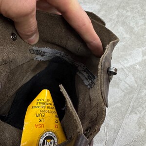 May include: Close-up of a brown leather boot interior. A yellow tag with the CAT logo and size information is visible. The boot has a worn appearance, with visible stitching and metal hardware.