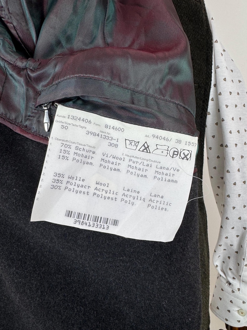 May include: Close-up of a dark green wool coat's interior, revealing a burgundy lining and a label with product information. The label includes details about the fabric composition, such as wool, mohair, and polyester.