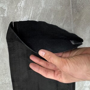 May include: A black leather sleeve or cuff featuring a textured exterior surface and a soft, matte black interior lining. The material appears flexible and durable, showing a natural grain pattern on the outer side and a smooth finish inside.