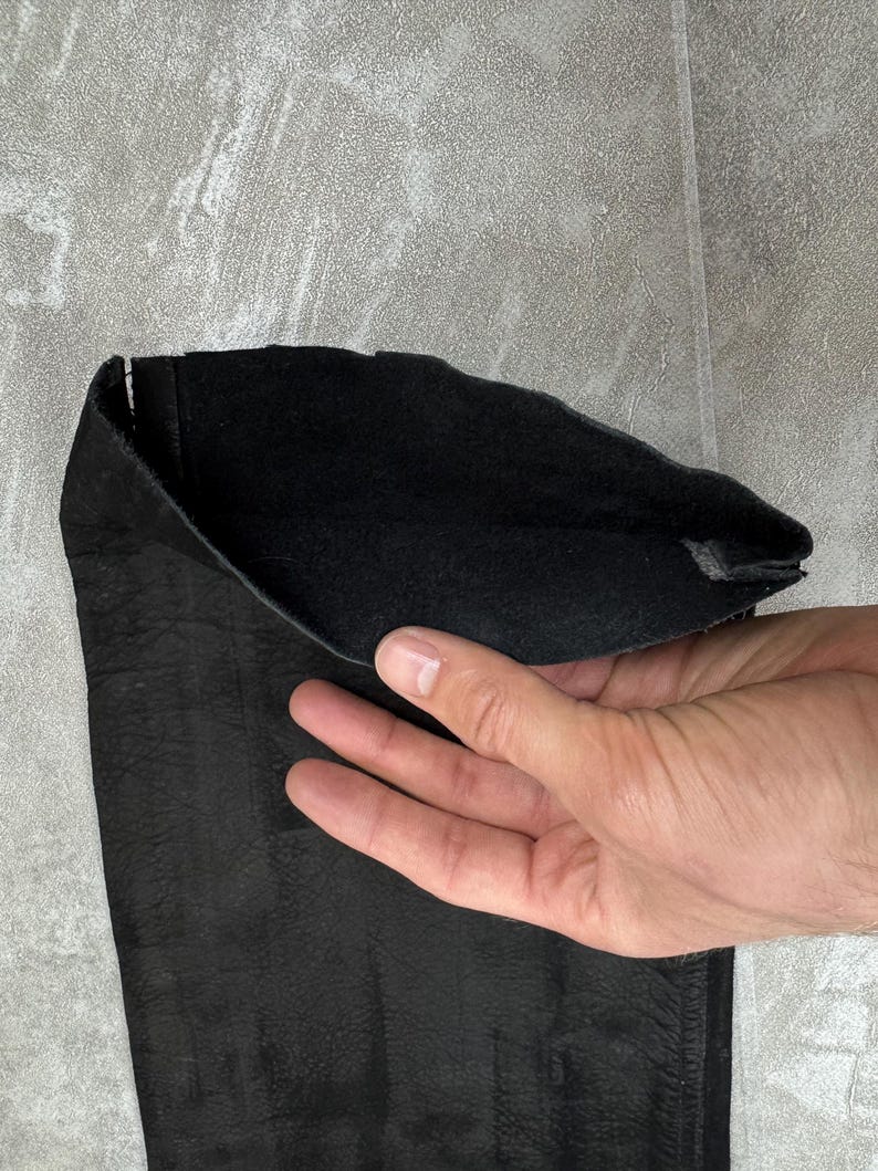 May include: A black leather sleeve or cuff featuring a textured exterior surface and a soft, matte black interior lining. The material appears flexible and durable, showing a natural grain pattern on the outer side and a smooth finish inside.